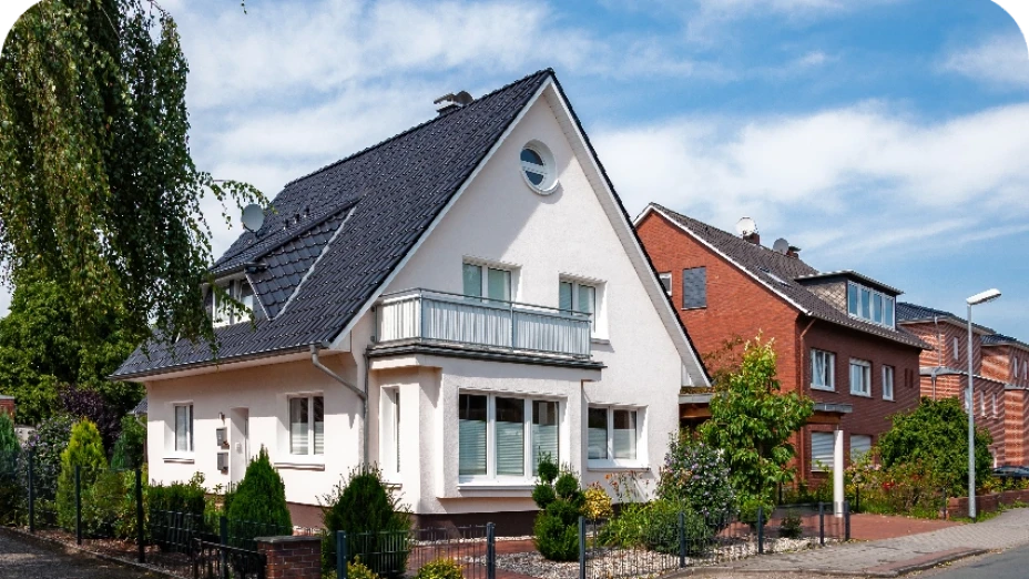 Weißes Einfamilienhaus mit dunklem Dach und Balkon an einer Wohnstraße